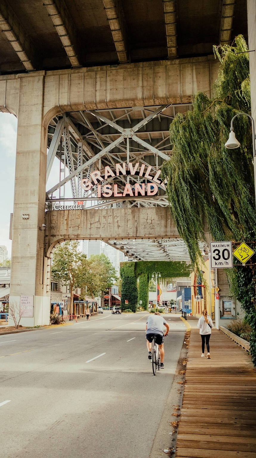 People walking and cycling under a bridge toward a sign that reads 