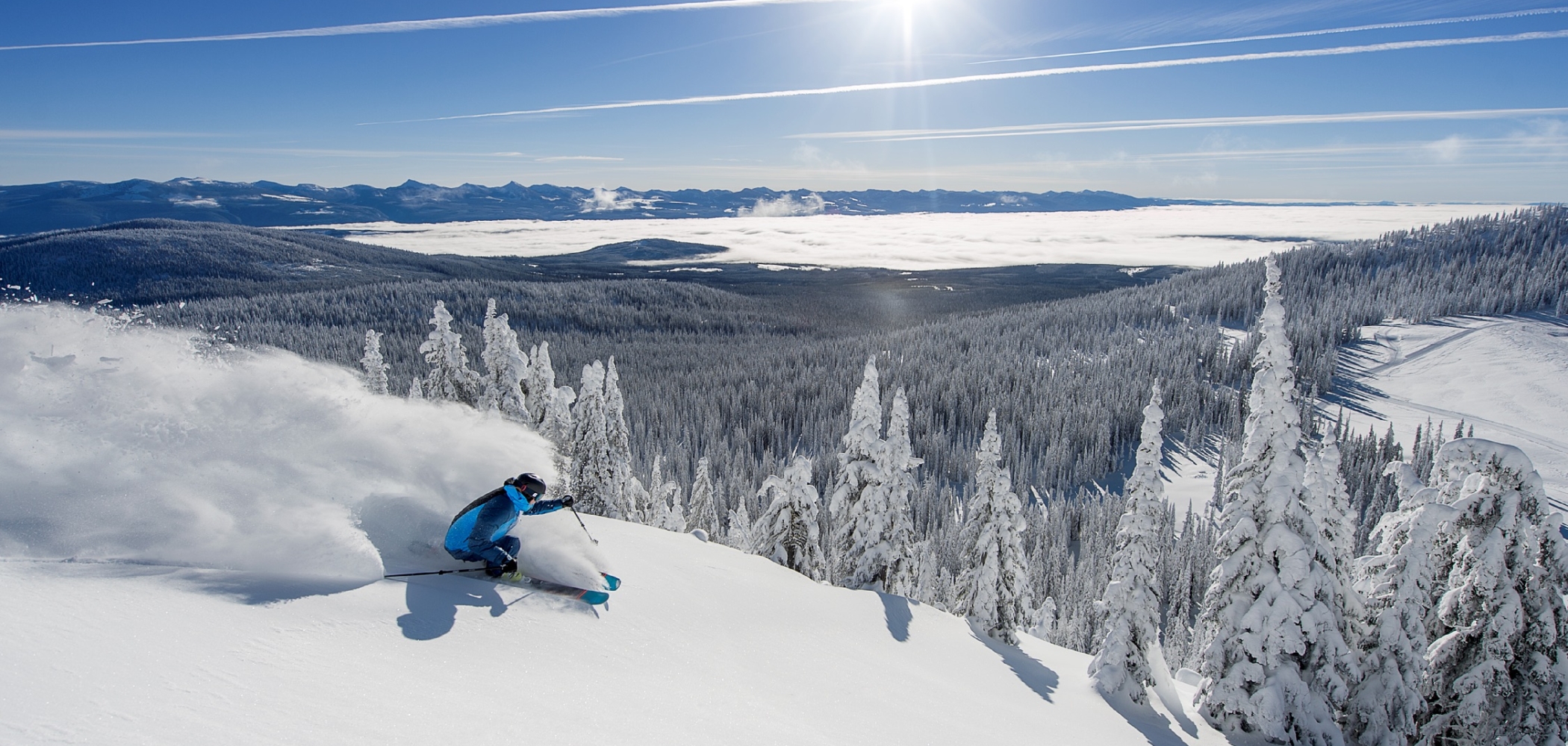 A skier takes large, sweeping powder turns on a bluebird day at Big White Ski Resort.